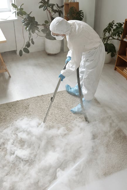 Close-up of a person's hands operating a yellow carpet cleaning machine in a room with a patterned, traditional-style rug featuring shades of beige, blue, and red. The machine appears to be a deep cle